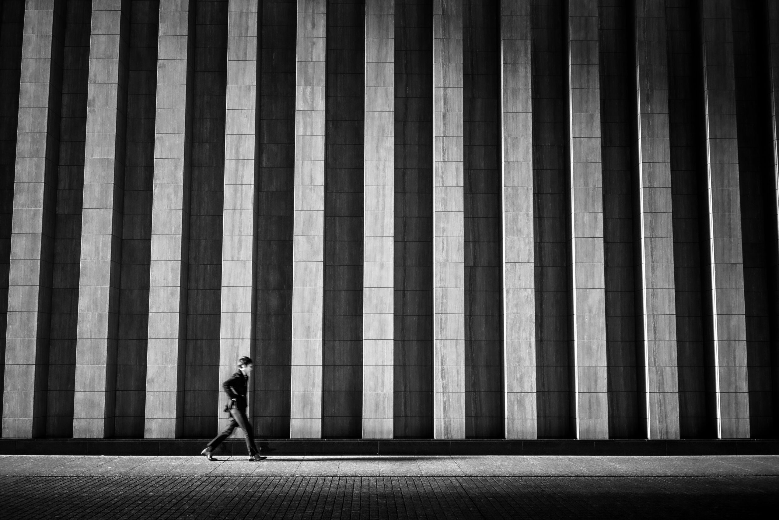 Grayscale photo of person walking on sidewalk Grayscale photo of person walking on sidewalk